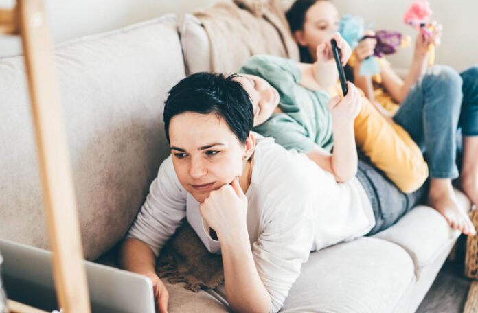 adult watching laptop on couch with child on back