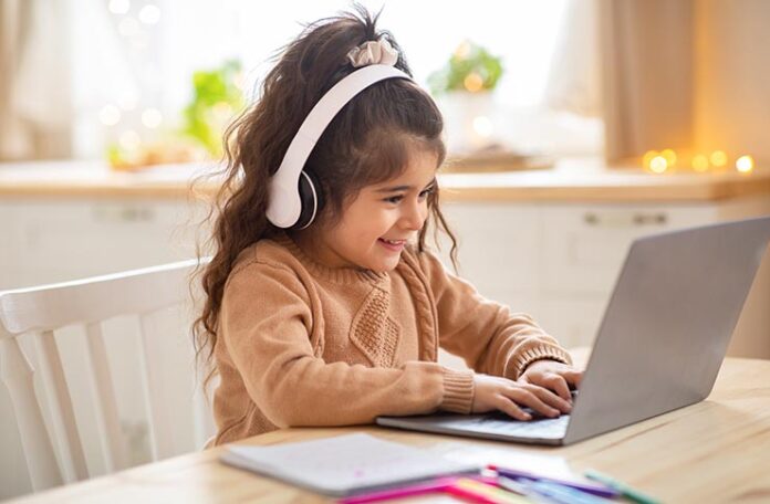 Cute,Little,Preschooler,Girl,In,Wireless,Headphones,Using,Laptop,At Young girl with headphones using laptop