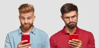 Two adult males viewing mobile phone screens with confused looks.