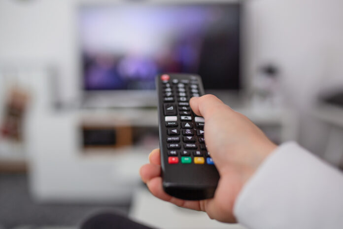 Watching TV and using remote controller. Hand with remote controller changing channels or opening apps on smart tv A hand holding a TV remote while searching streaming services for new movies to watch