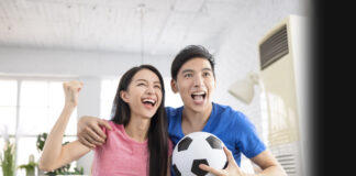 Young couple with soccer ball celebrating while streaming the Women’s World Cup on TV