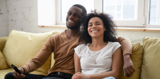 Happy couple eating popcorn on the couch while streaming the latest TV series
