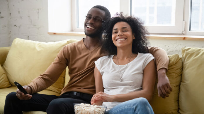 Overjoyed biracial couple have fun watching TV together Happy couple eating popcorn on the couch while streaming the latest TV series