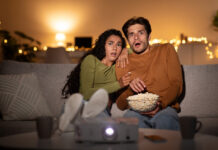 Scared couple eating popcorn on the couch while streaming a horror movie
