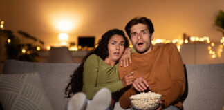 Scared couple eating popcorn on the couch while streaming a horror movie