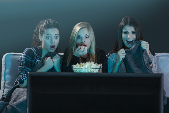 Three scared teenage girls streaming a horror movie on TV