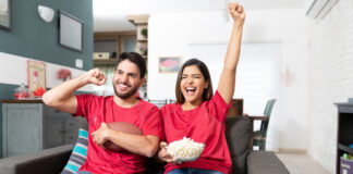 Young couple celebrating while watching college football on TV at home