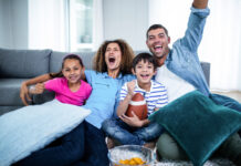 A family sitting on the couch at home while watching NFL football on TV