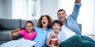 A family sitting on the couch at home while watching NFL football on TV