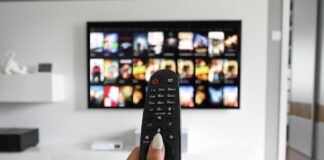 A woman’s hand holding up a TV remote in front of a television screen