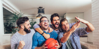 A group of male friends watching the March Madness men’s basketball tournament on TV at home.