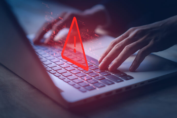 Hands typing on a laptop with an icon of a warning label depicting illegal activities.