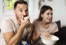 Man and woman eating popcorn at home while streaming the latest blockbuster movies