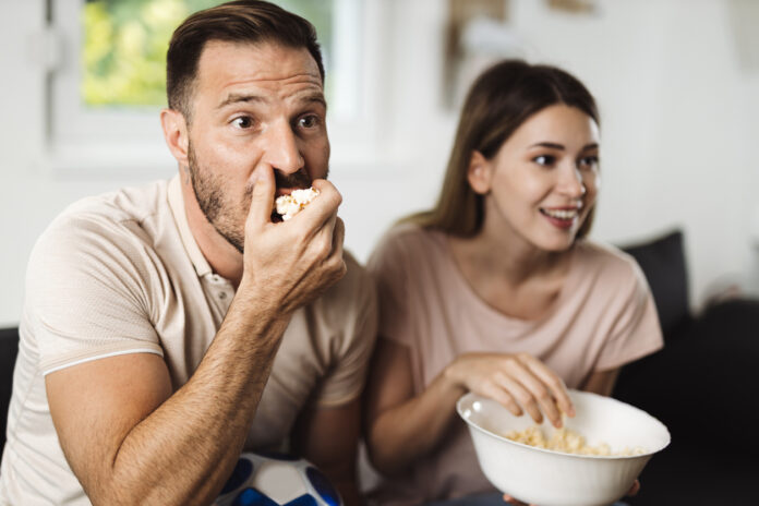 Man and woman eating popcorn at home while streaming the latest blockbuster movies