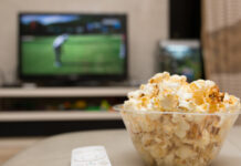 A bowl of popcorn and a TV remote with a TV broadcasting a golf tournament in the background.