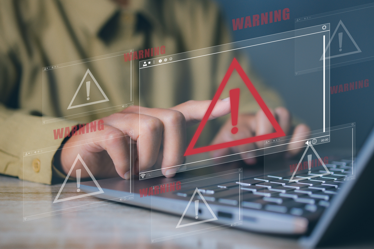 A user typing on their laptop and hazarrd signs tabs popping up on the fore ground of the image. 