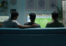 Common Illegal Sports Streaming Sites to Avoid Three young men sitting on the sofa while streaming a soccer match on TV at home.