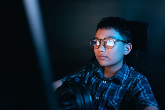 Kids’ Safety oung kid on the computer playing games, watching entertainment or browsing the online digital internet, wearing glasses and dark background theme