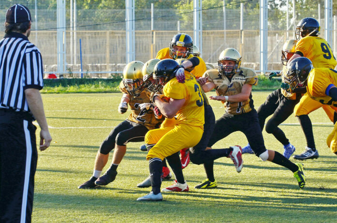 people playing american football with referee on the field during daytime.