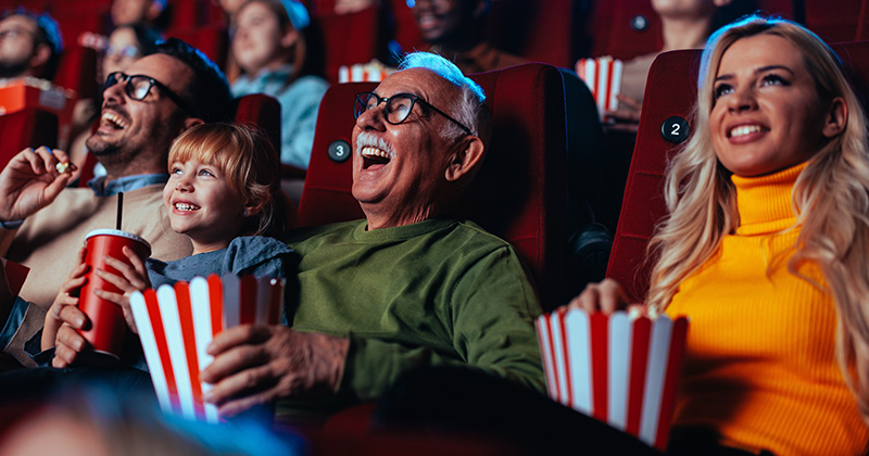 summer_movies A crowd of happy spectators are in the movie, sitting in the chairs laughing at the movie they are watching and enjoying popcorn and drinks.