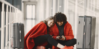 Is an Unsecured Public Wi-Fi Network Safe for Streaming? Two happy people in red waiting in airport with luggage sharing wifi on mobile device